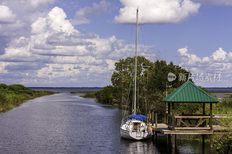 佛罗里达州圣克劳德(St Cloud)和基西米(Kissimmee)之间的一个湖泊出口处，一艘帆船停泊在一个码头上，码头上有一个露台下的休息区